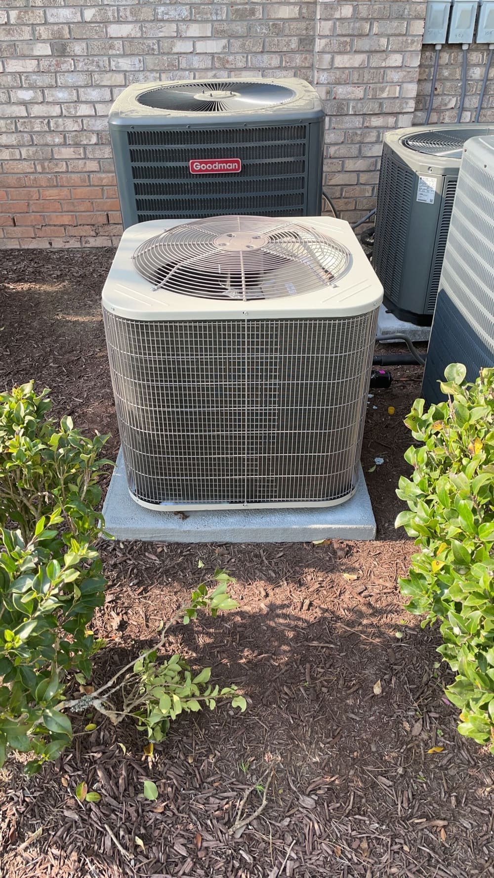 Two outdoor condensers on pads beside a brick wall