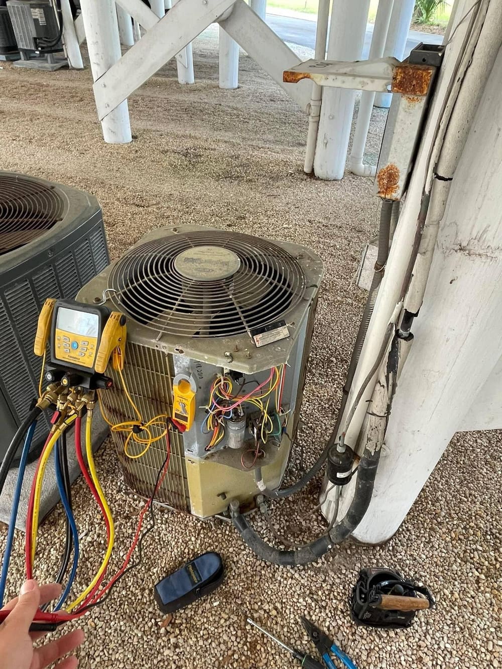 Outdoor condenser with manifold gauges connected, set under a raised house