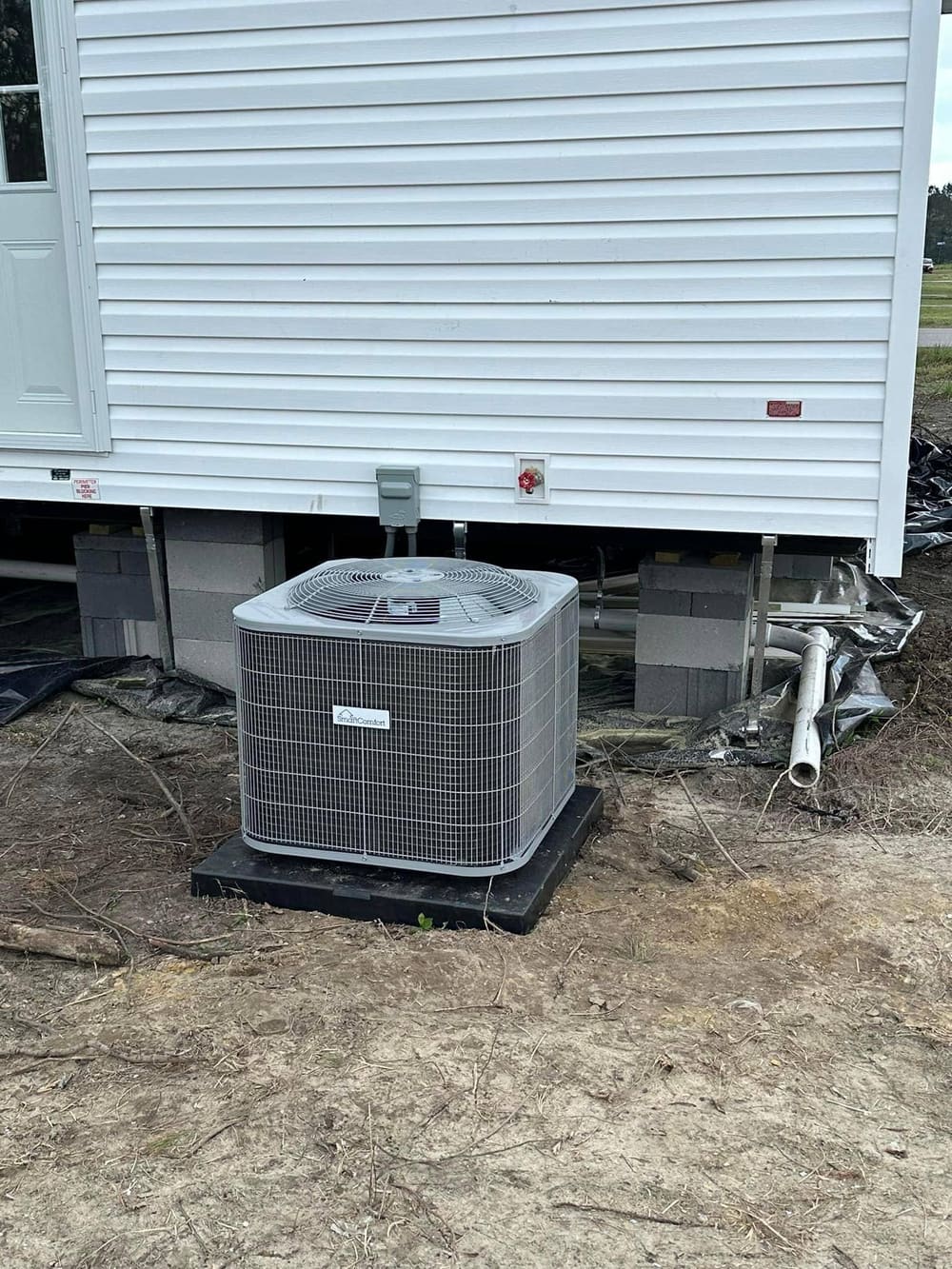New outdoor condenser on a pad beside a white mobile home