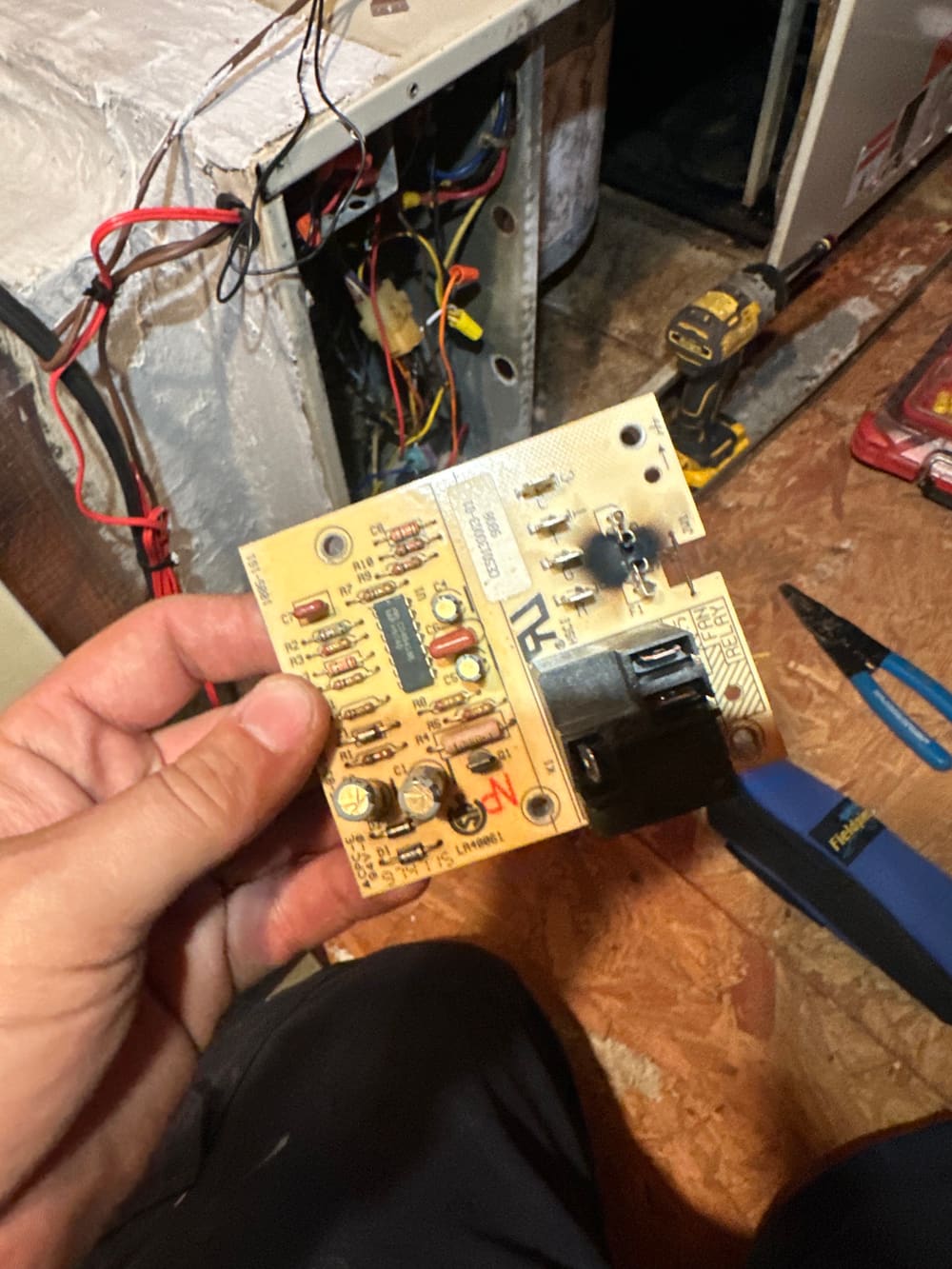 Furnace control board held in a gloved hand during a repair
