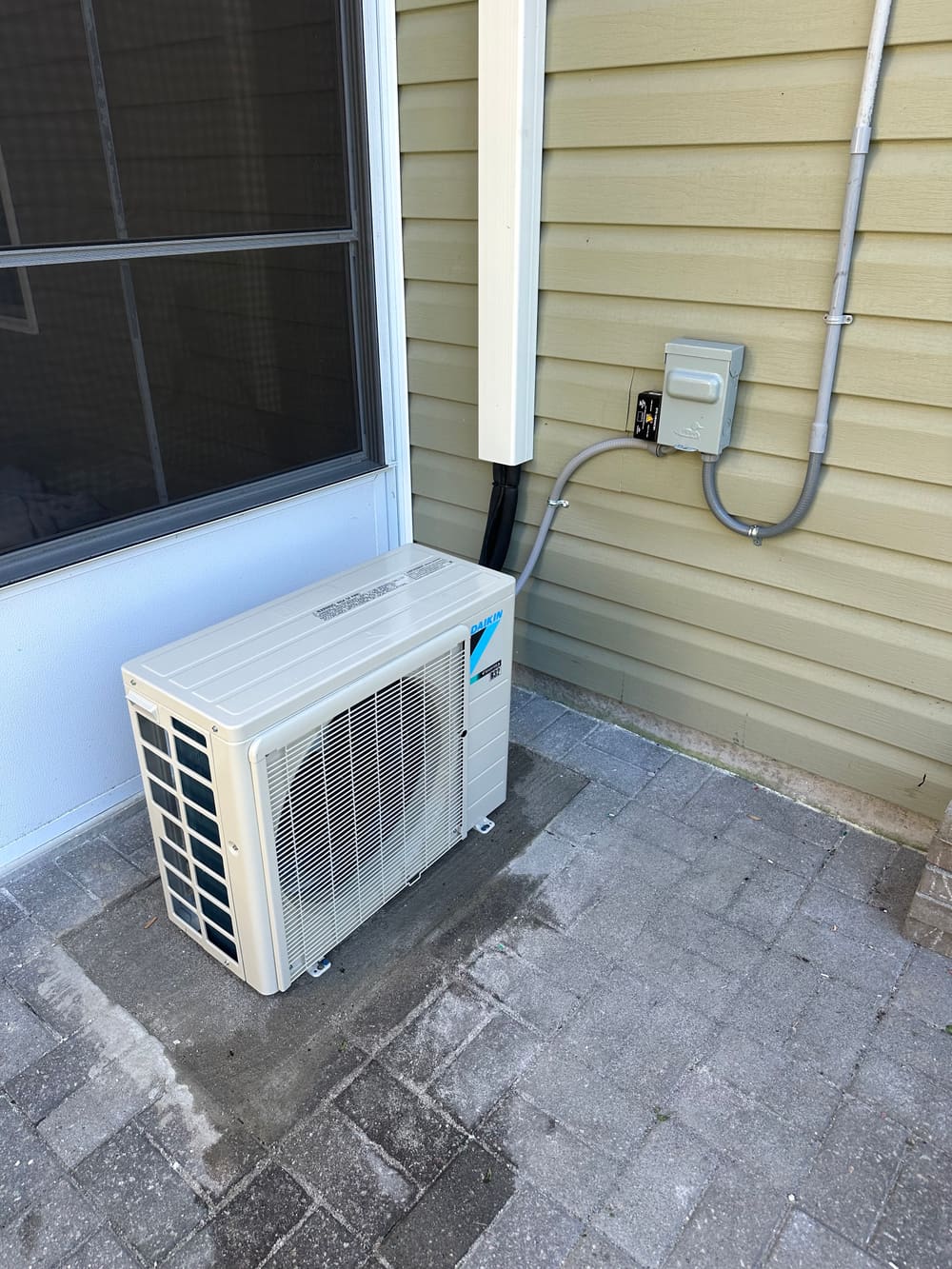 Daikin mini-split outdoor unit on a paver pad beside a house
