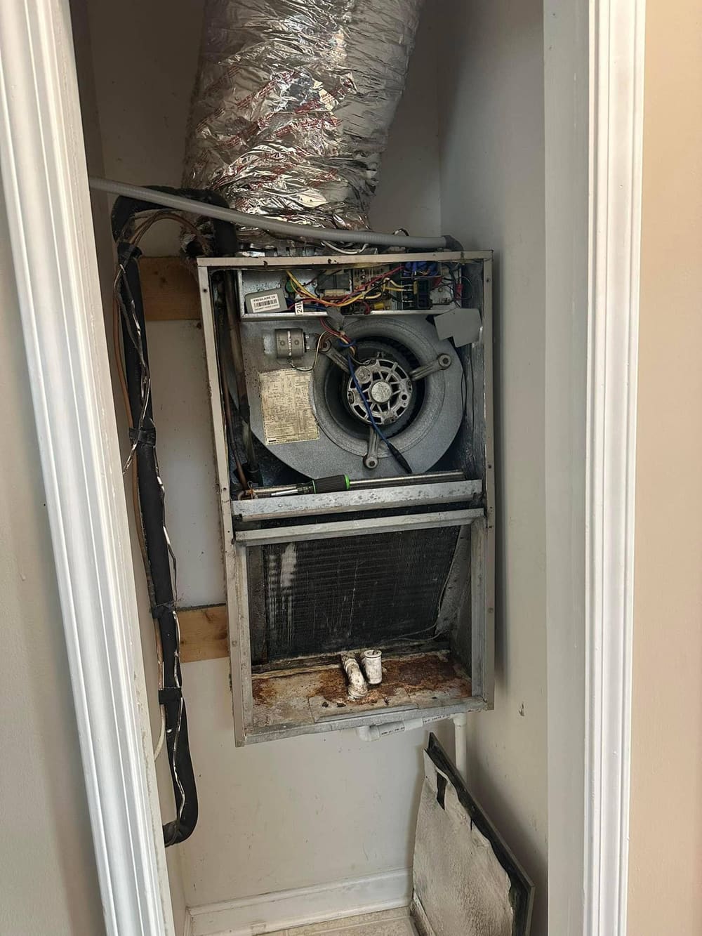 Furnace cabinet open in a closet with the blower and wiring exposed