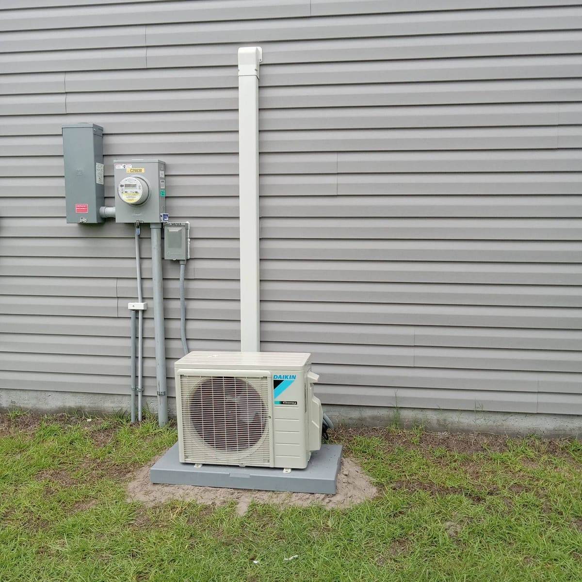 Daikin mini-split outdoor unit on a pad beside gray siding