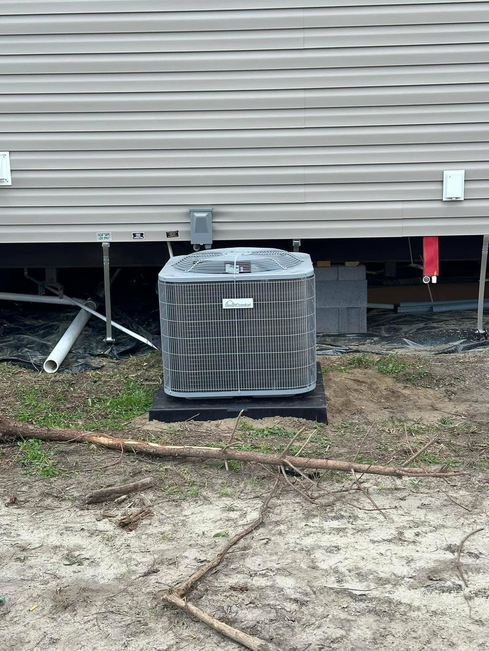 New outdoor condenser on a pad beside gray mobile home skirting