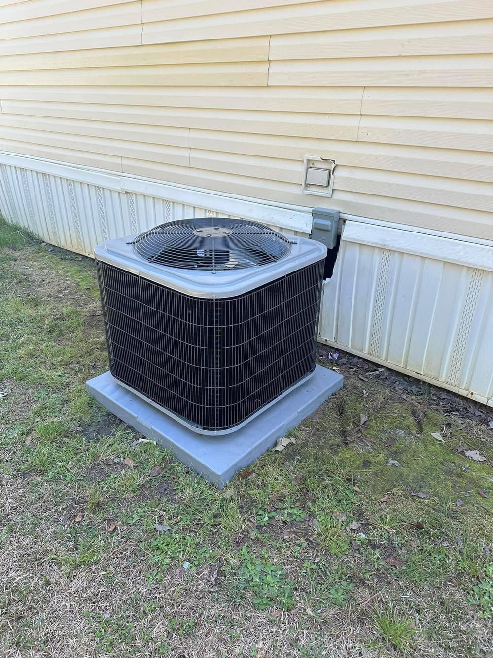 New outdoor condenser on a fresh pad beside a mobile home