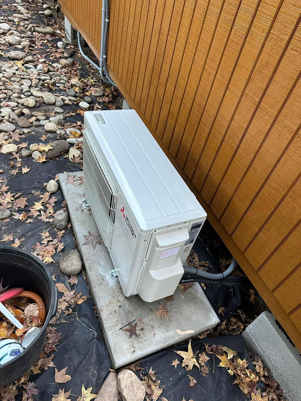 Ductless mini-split outdoor unit on a pad against a wood-clad wall