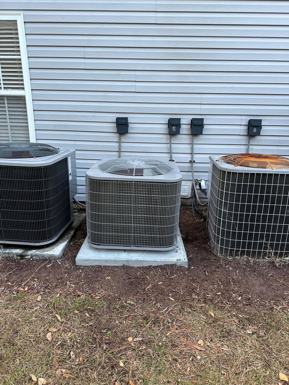 Three outdoor condensers side by side on pads along a house wall