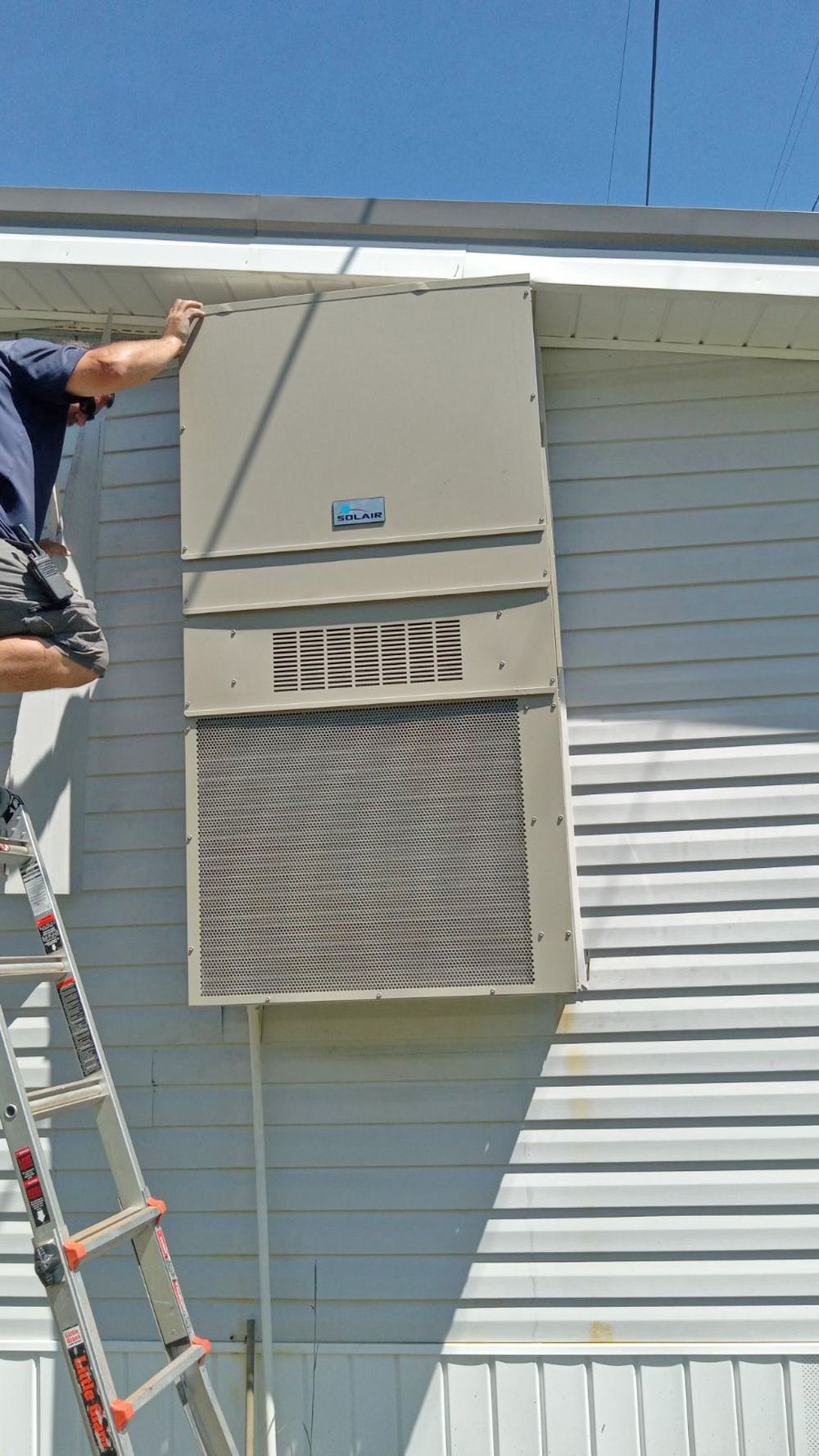 Arctic Air technician installing exterior wall unit on ladder